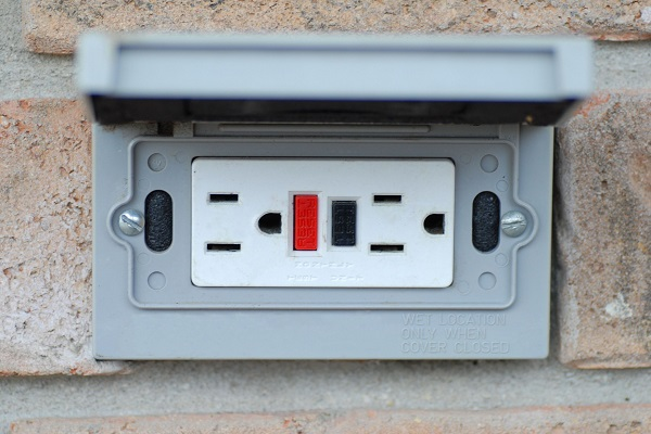 An outdoor GFCI outlet positioned horizontally on a brick wall